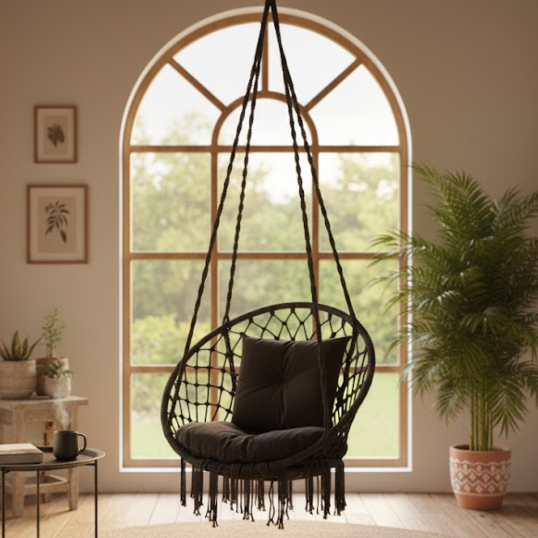 Black macrame hanging chair with cushions in a room with large arched window and plants.